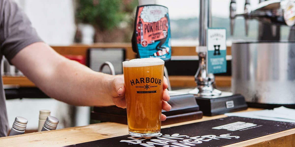 A barman handing over a pint of Harbour Ellensberg at The Working Boat pub in Falmouth, Cornwall